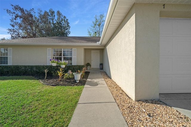 view of exterior entry with a yard, an attached garage, and stucco siding