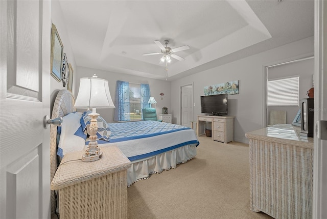 bedroom featuring a raised ceiling, a ceiling fan, and light colored carpet