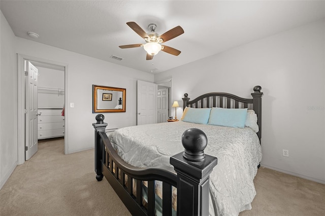 bedroom with a ceiling fan, a walk in closet, visible vents, and light carpet