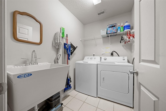 washroom with laundry area, light tile patterned floors, visible vents, washing machine and clothes dryer, and a sink