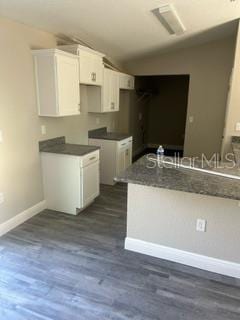 kitchen with lofted ceiling, dark countertops, white cabinetry, baseboards, and dark wood-style flooring