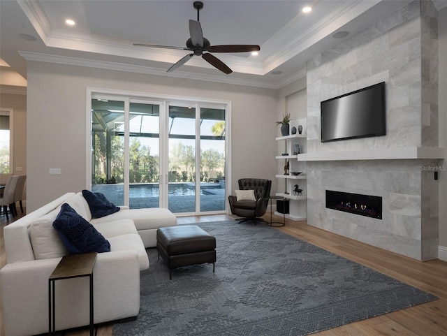 living area with a fireplace, crown molding, a tray ceiling, and wood finished floors