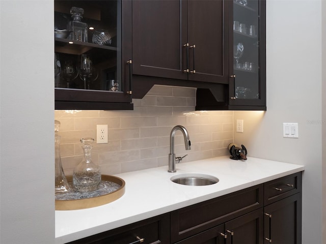 kitchen with a sink, dark brown cabinetry, light countertops, glass insert cabinets, and backsplash