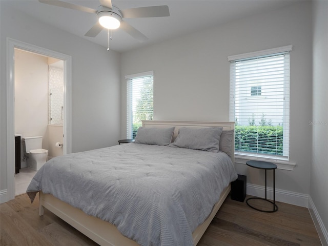 bedroom with baseboards, ensuite bath, wood finished floors, and a ceiling fan