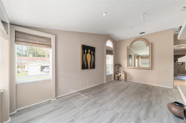 unfurnished living room featuring baseboards, visible vents, vaulted ceiling, and light wood finished floors