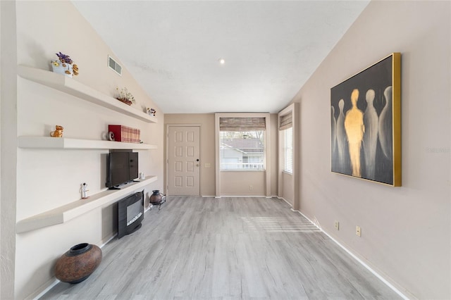 interior space with light wood-type flooring, baseboards, visible vents, and vaulted ceiling