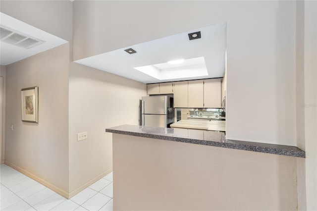 kitchen with a skylight, visible vents, a raised ceiling, freestanding refrigerator, and a peninsula