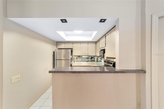 kitchen featuring light tile patterned floors, a peninsula, appliances with stainless steel finishes, dark countertops, and a raised ceiling