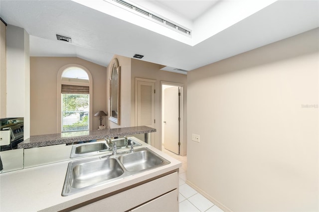 kitchen featuring light tile patterned floors, a sink, visible vents, white cabinets, and vaulted ceiling