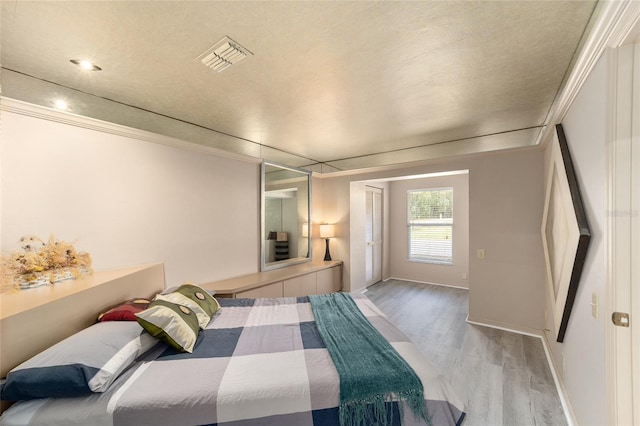 bedroom featuring ornamental molding, light wood-type flooring, visible vents, and baseboards