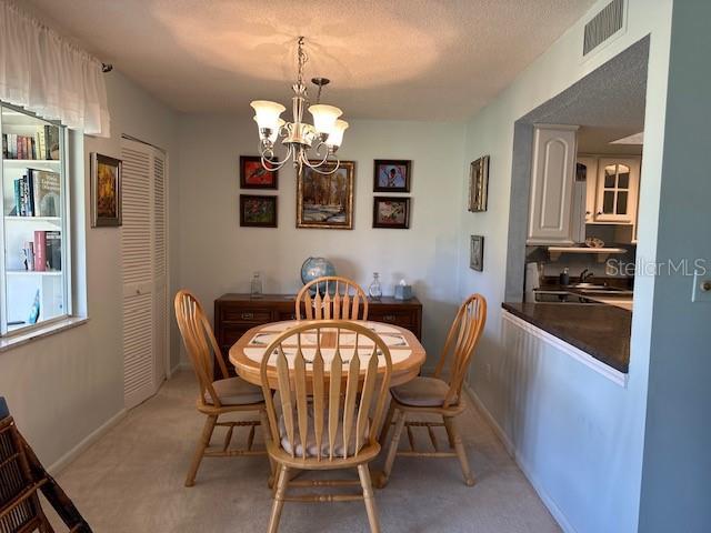 dining area featuring a chandelier, light colored carpet, visible vents, and baseboards