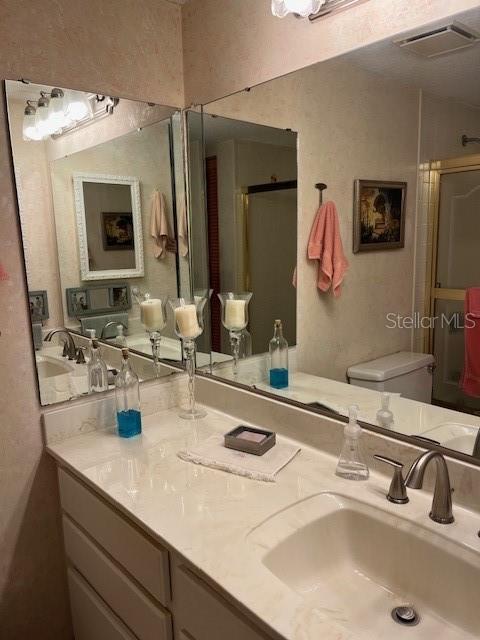 full bathroom with toilet, vanity, a shower stall, and visible vents