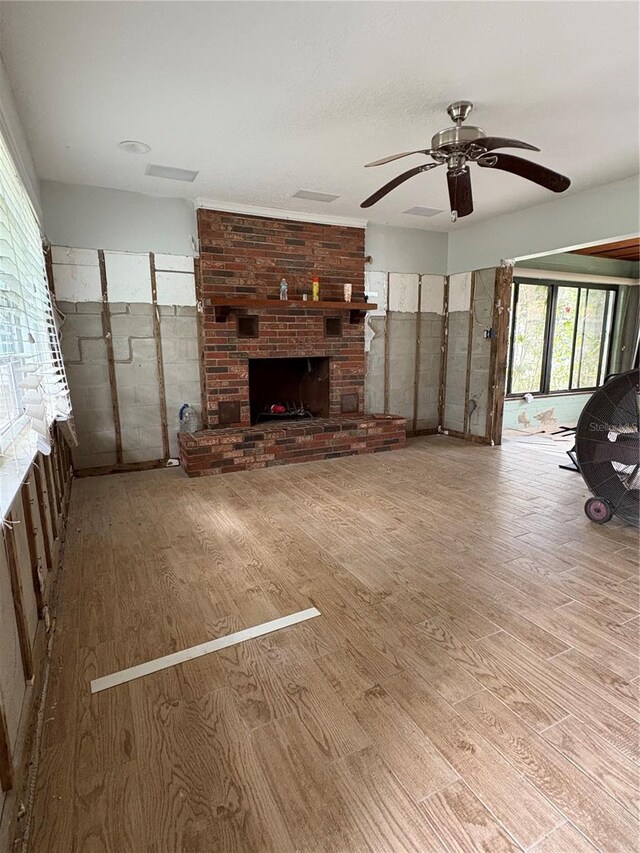 unfurnished living room featuring ceiling fan, a brick fireplace, and wood finished floors