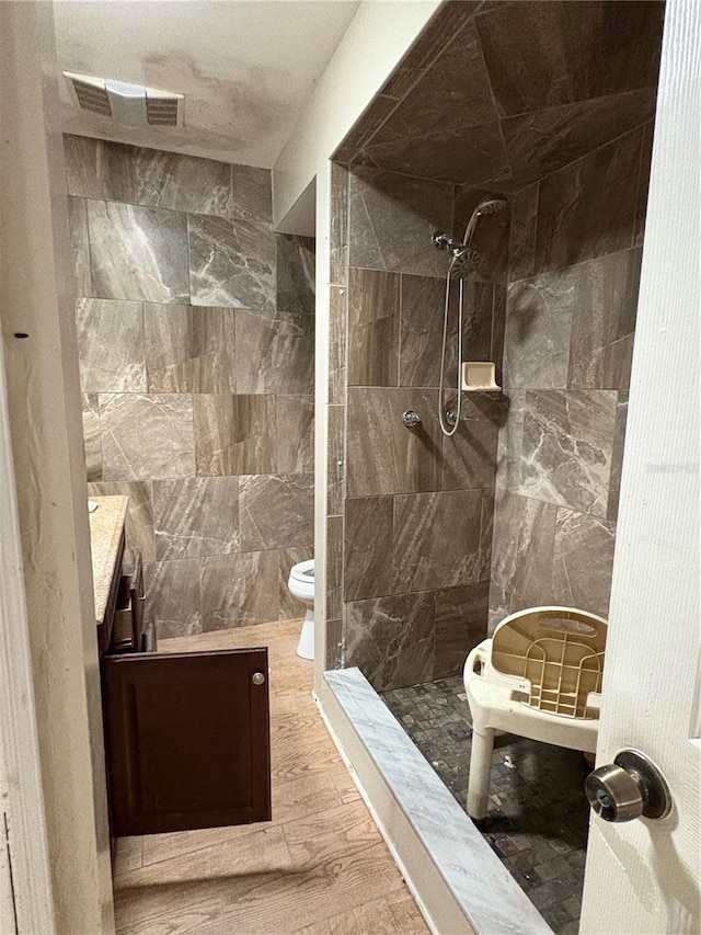 bathroom with visible vents, toilet, tile walls, tiled shower, and vanity