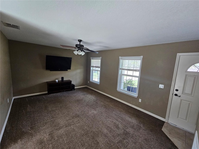 unfurnished living room featuring dark colored carpet, visible vents, a ceiling fan, a textured ceiling, and baseboards