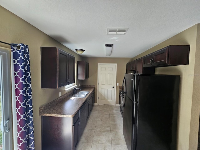 kitchen featuring light tile patterned floors, visible vents, freestanding refrigerator, a sink, and dark brown cabinets