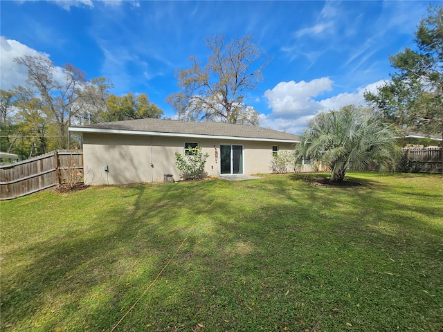 rear view of house with a lawn, fence, and stucco siding