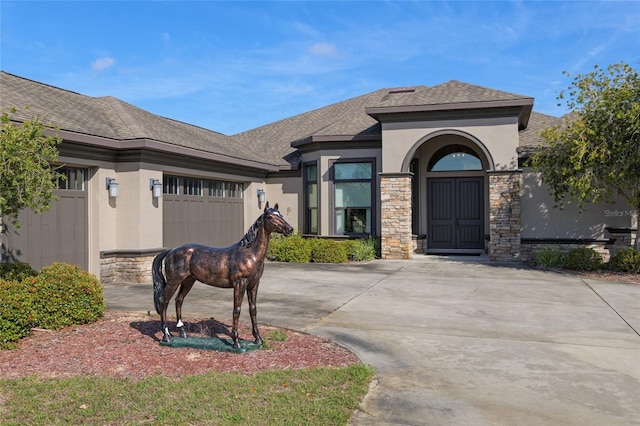 view of front of home featuring an attached garage, a shingled roof, concrete driveway, stone siding, and stucco siding