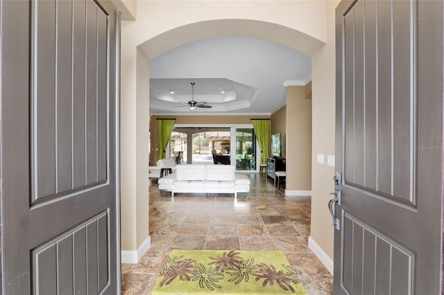 entryway featuring baseboards, arched walkways, a raised ceiling, a ceiling fan, and ornamental molding