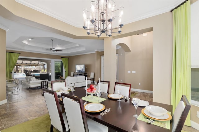 dining area with baseboards, a raised ceiling, arched walkways, ornamental molding, and ceiling fan with notable chandelier