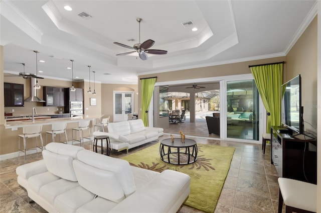 living area featuring ornamental molding, a tray ceiling, visible vents, and arched walkways