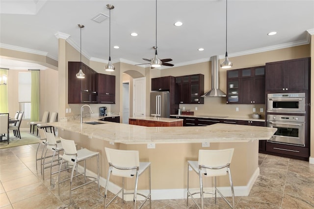 kitchen with arched walkways, a peninsula, a sink, wall chimney range hood, and appliances with stainless steel finishes