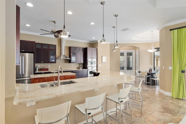 kitchen featuring a breakfast bar area, a sink, ornamental molding, wall chimney range hood, and freestanding refrigerator