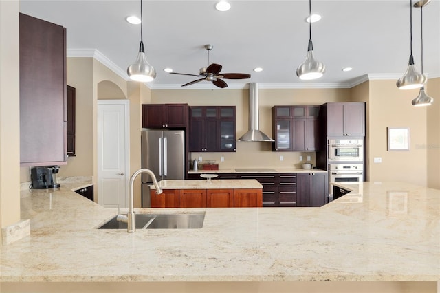 kitchen with arched walkways, stainless steel appliances, a sink, light stone countertops, and wall chimney exhaust hood