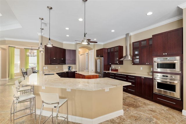 kitchen with a center island, a breakfast bar area, stainless steel appliances, a sink, and wall chimney range hood