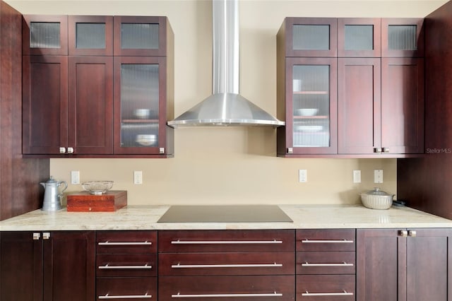 kitchen with wall chimney range hood, glass insert cabinets, black electric cooktop, and dark brown cabinets