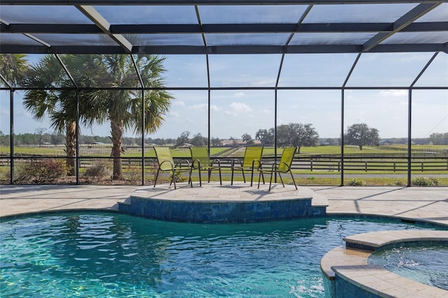 view of pool featuring a pool with connected hot tub, glass enclosure, a patio, and a rural view