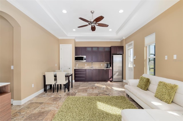 living room featuring baseboards, a raised ceiling, arched walkways, ornamental molding, and recessed lighting