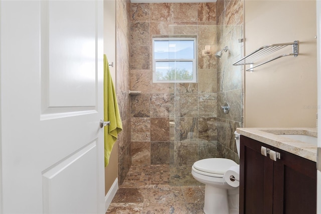 bathroom with stone finish flooring, tiled shower, vanity, and toilet