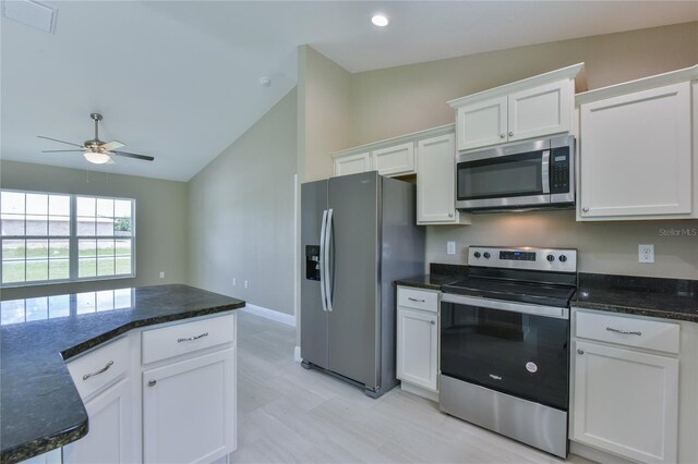 kitchen with lofted ceiling, visible vents, white cabinets, appliances with stainless steel finishes, and dark stone countertops