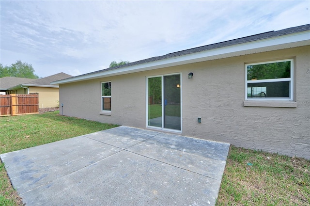 rear view of property with a patio, a lawn, fence, and stucco siding