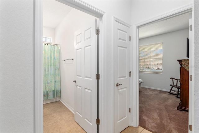 hallway with light carpet, light tile patterned floors, and baseboards