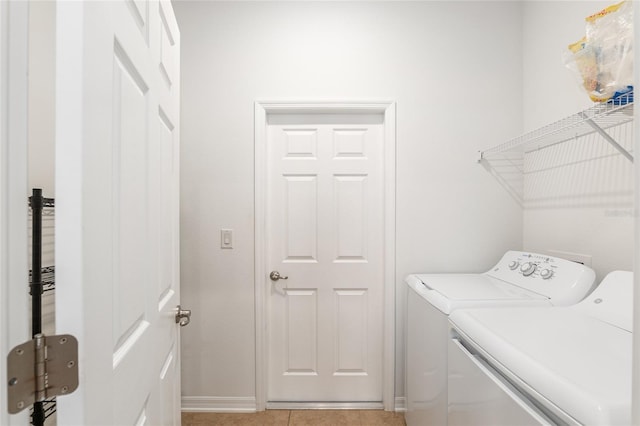 clothes washing area featuring laundry area, baseboards, light tile patterned flooring, and washing machine and clothes dryer