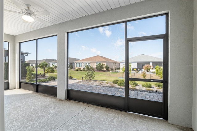 unfurnished sunroom featuring a residential view and a ceiling fan