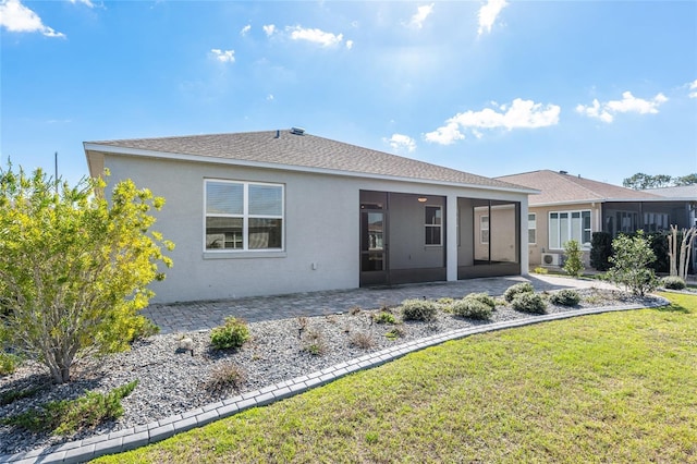 rear view of property featuring a shingled roof, a sunroom, a yard, stucco siding, and a patio area