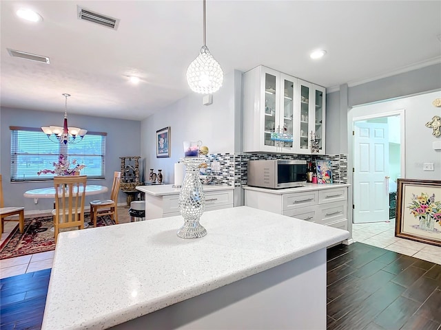 kitchen with stainless steel microwave, backsplash, visible vents, and an inviting chandelier