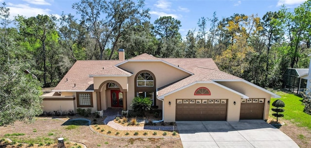 mediterranean / spanish house with a chimney, stucco siding, a shingled roof, concrete driveway, and an attached garage