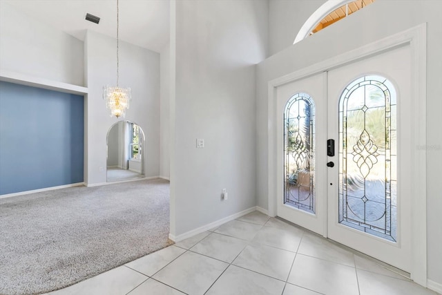 entrance foyer with a towering ceiling, arched walkways, light colored carpet, and french doors