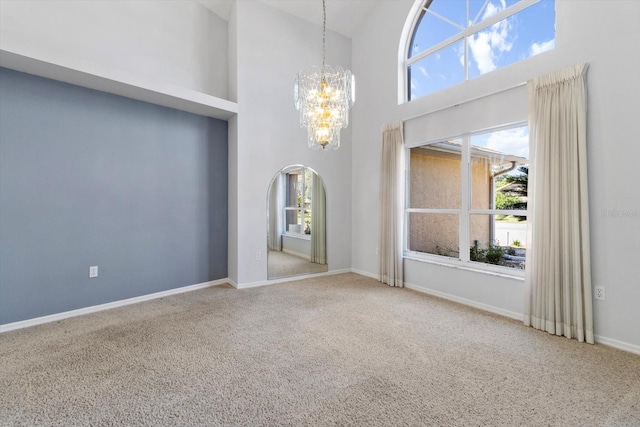 spare room featuring arched walkways, a notable chandelier, carpet flooring, high vaulted ceiling, and baseboards