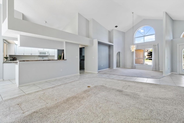 unfurnished living room featuring light tile patterned floors, high vaulted ceiling, baseboards, and light colored carpet