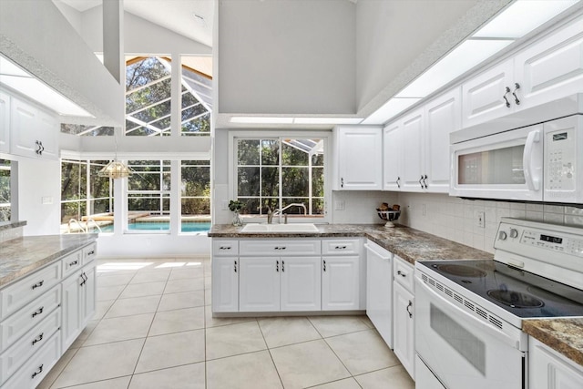 kitchen with a towering ceiling, white appliances, decorative backsplash, and a sink