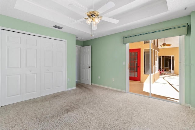 unfurnished bedroom with visible vents, a tray ceiling, and carpet flooring