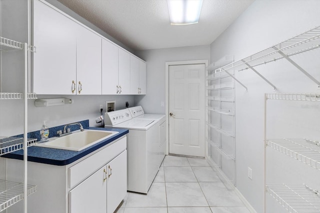 laundry area featuring cabinet space, light tile patterned flooring, a sink, a textured ceiling, and independent washer and dryer