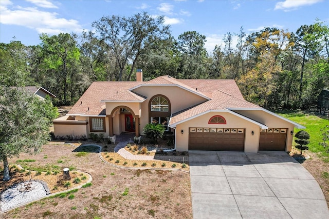 mediterranean / spanish-style house featuring driveway, a chimney, an attached garage, and stucco siding