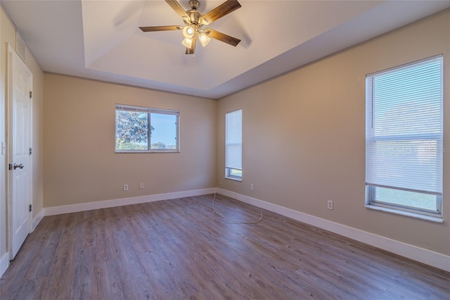 spare room featuring ceiling fan, a tray ceiling, baseboards, and wood finished floors