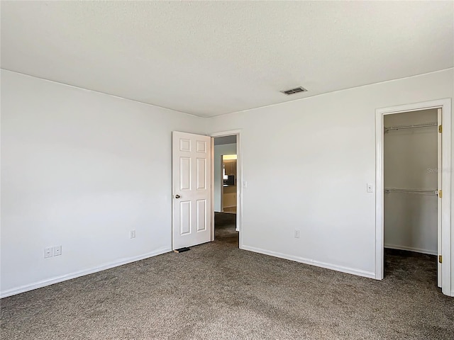 unfurnished bedroom with a textured ceiling, visible vents, baseboards, a spacious closet, and carpet